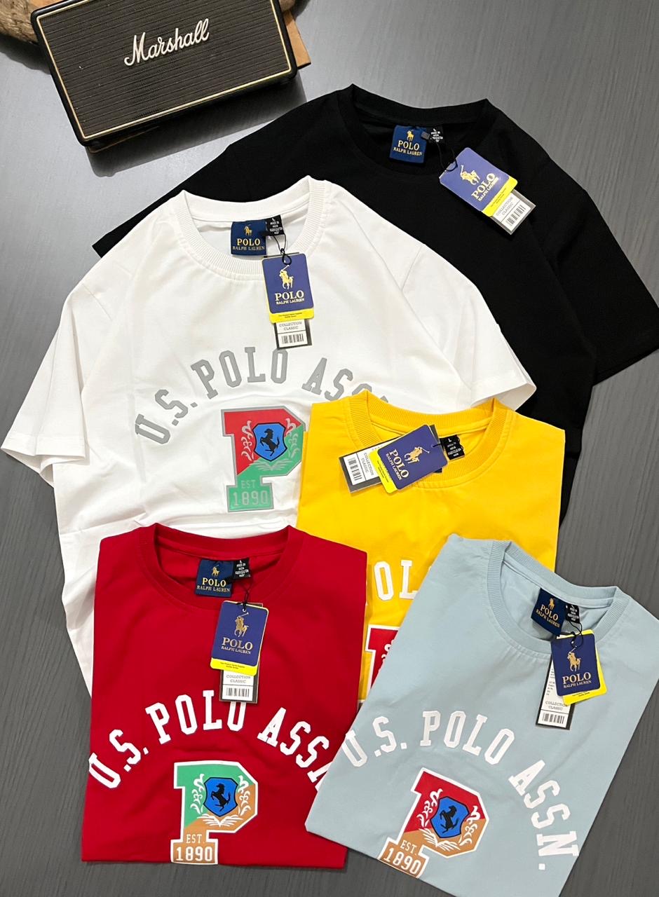 Five U.S. Polo Assn. t-shirts in white, black, yellow, red, and blue on a gray surface.