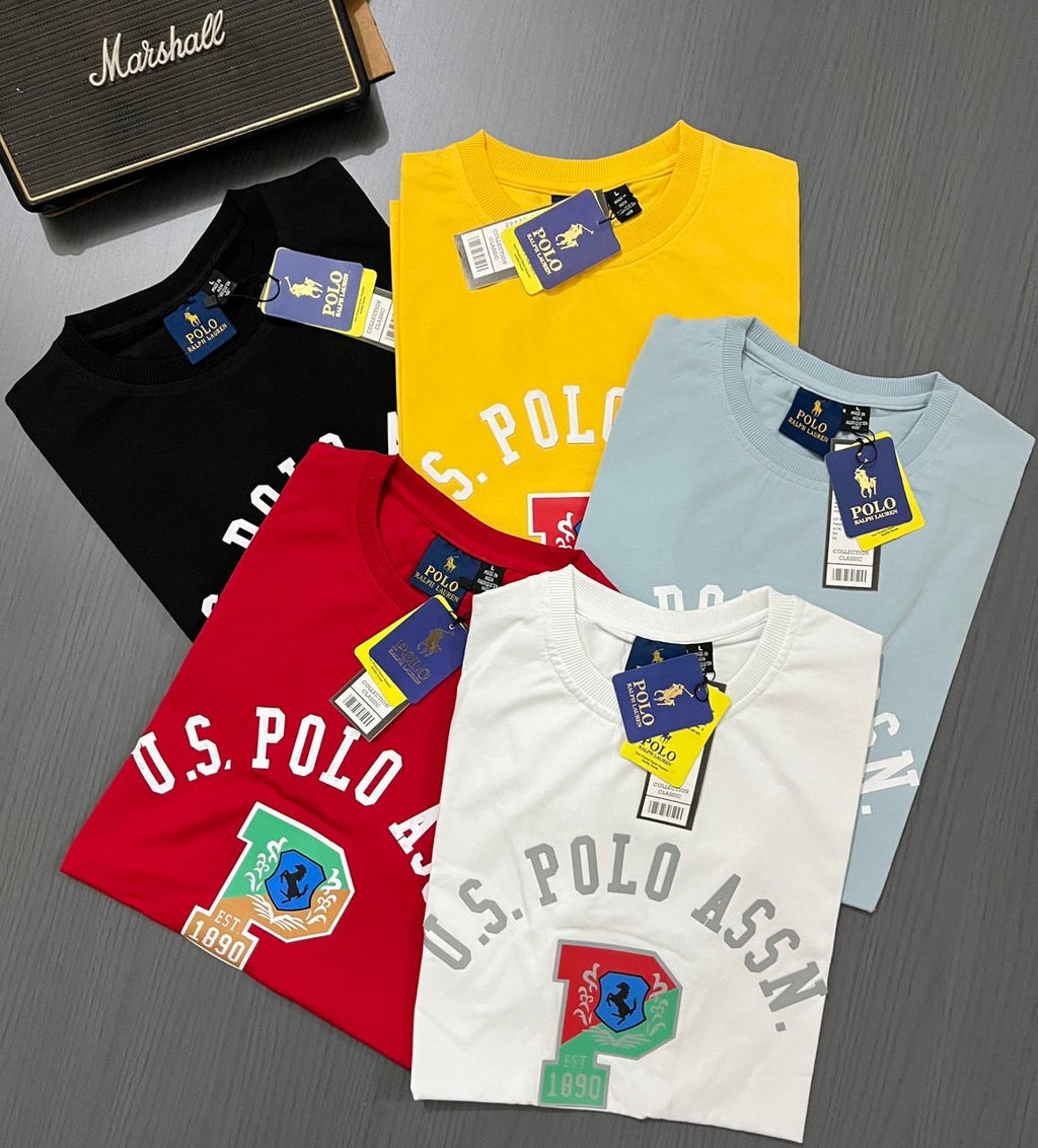 Five polo shirts in black, yellow, red, white, and blue with tags on a gray surface.